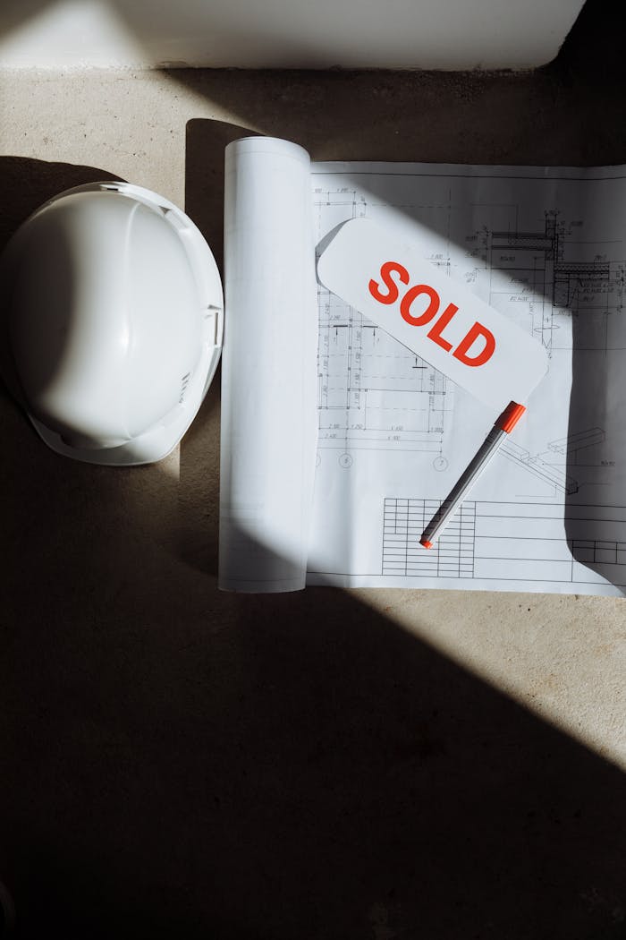 Blueprints with a sold sign and hard hat on a sunlit surface, symbolizing real estate success.